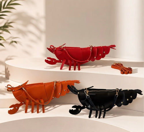 Three lobster-shaped shoulder bags in red, orange, and black, displayed on white tiered platforms with a small matching strap set.