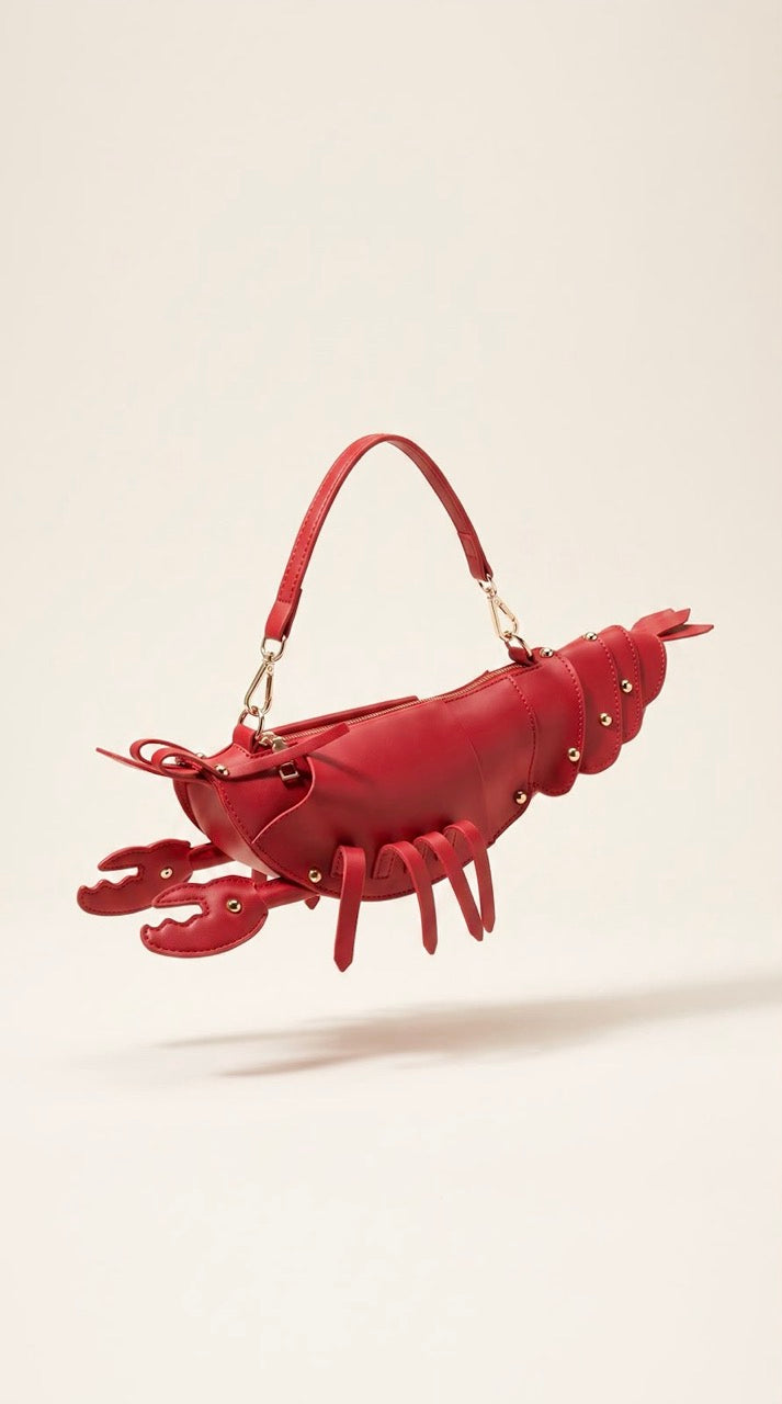 A red lobster-shaped handbag with a top handle and gold-tone hardware, photographed against a plain light beige studio background.